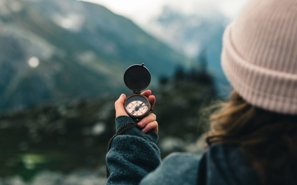 A person holding a compass overlooking the mountains, symbolizing finding life direction with a life coach for clarity and direction at Pam Landolt Green Coaching, LLC.
